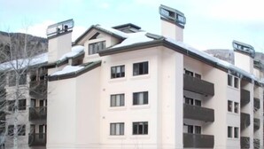 A multi-story building with a flat roof, a snow-covered ground, and a wooden fence in the foreground.