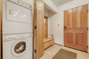A laundry room with stacked washers and dryers, a wooden bench, and a door.