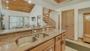 A modern kitchen with a granite countertop, stainless steel sink, wooden cabinets, and a spiral staircase.