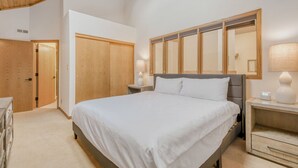 A bedroom with a large bed, wooden wardrobe, bedside tables with lamps, and a wooden ceiling.