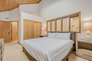 Un dormitorio con una cama grande, un armario de madera, mesitas de noche con lámparas y techo de madera.