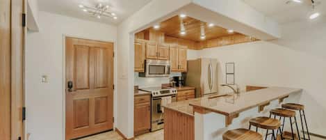 Une cuisine moderne avec des meubles en bois, des appareils électroménagers en acier inoxydable et un coin bar avec des tabourets.