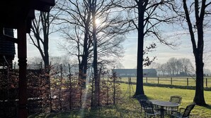 A patio area with a table and chairs, surrounded by trees and a view of a distant building. - Forest Villa, Rural Twente (Den Ham)