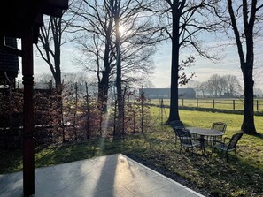 A patio area with a table and chairs, surrounded by trees and a view of a distant building. - Forest Villa, Rural Twente (Den Ham)