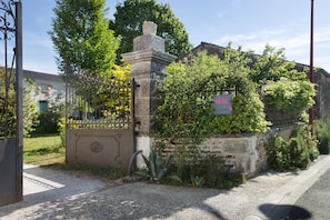 A gated entrance with a stone pillar, a signboard, and a building with a green door.