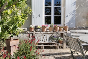 A stone bench, a wooden table, and potted plants in front of a building with a white door and windows. - Idyl – Guest Room in an Artists’ Home (Migré)