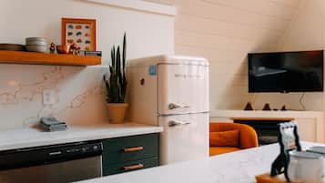 A kitchen with a white refrigerator, a dishwasher, a marble countertop, a plant, and a television mounted on the wall.
