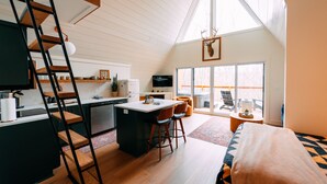 Un espace de vie de style « loft » comprenant une cuisine, un coin repas, une grande fenêtre et un escalier.