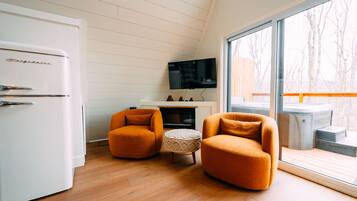 A modern kitchen with a white refrigerator, two orange armchairs, a small round ottoman, and a flat-screen TV mounted on the wall.