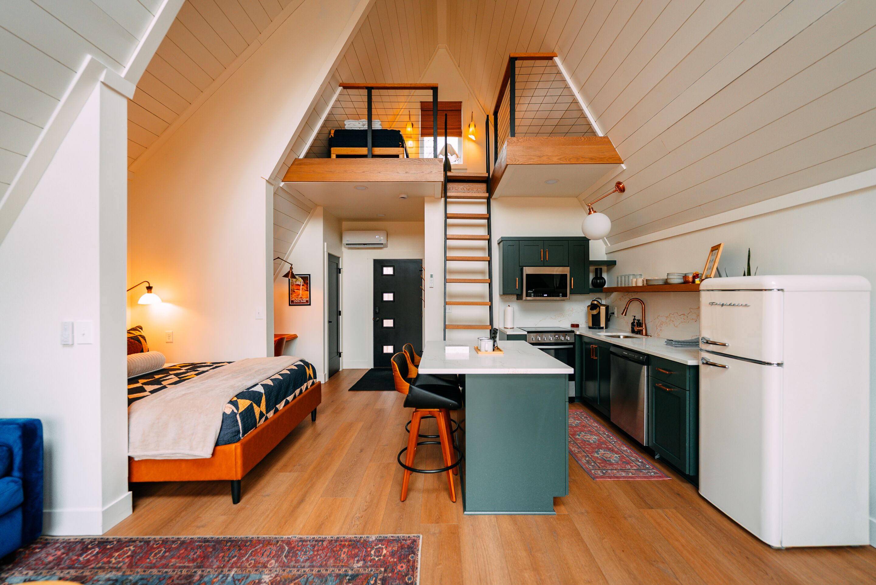 A loft-style bedroom with a bed, a desk, and a staircase leading to an upper level.