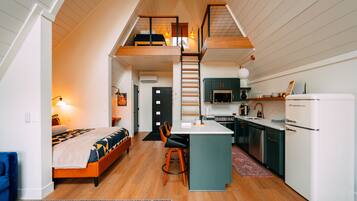 A loft-style bedroom with a bed, a desk, and a staircase leading to an upper level.