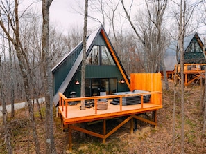 A cabin with a sloped roof, a deck with outdoor seating, and a large window. - Hickory Hollow | Hocking Hills, Hot Tub, Romantic (McArthur)