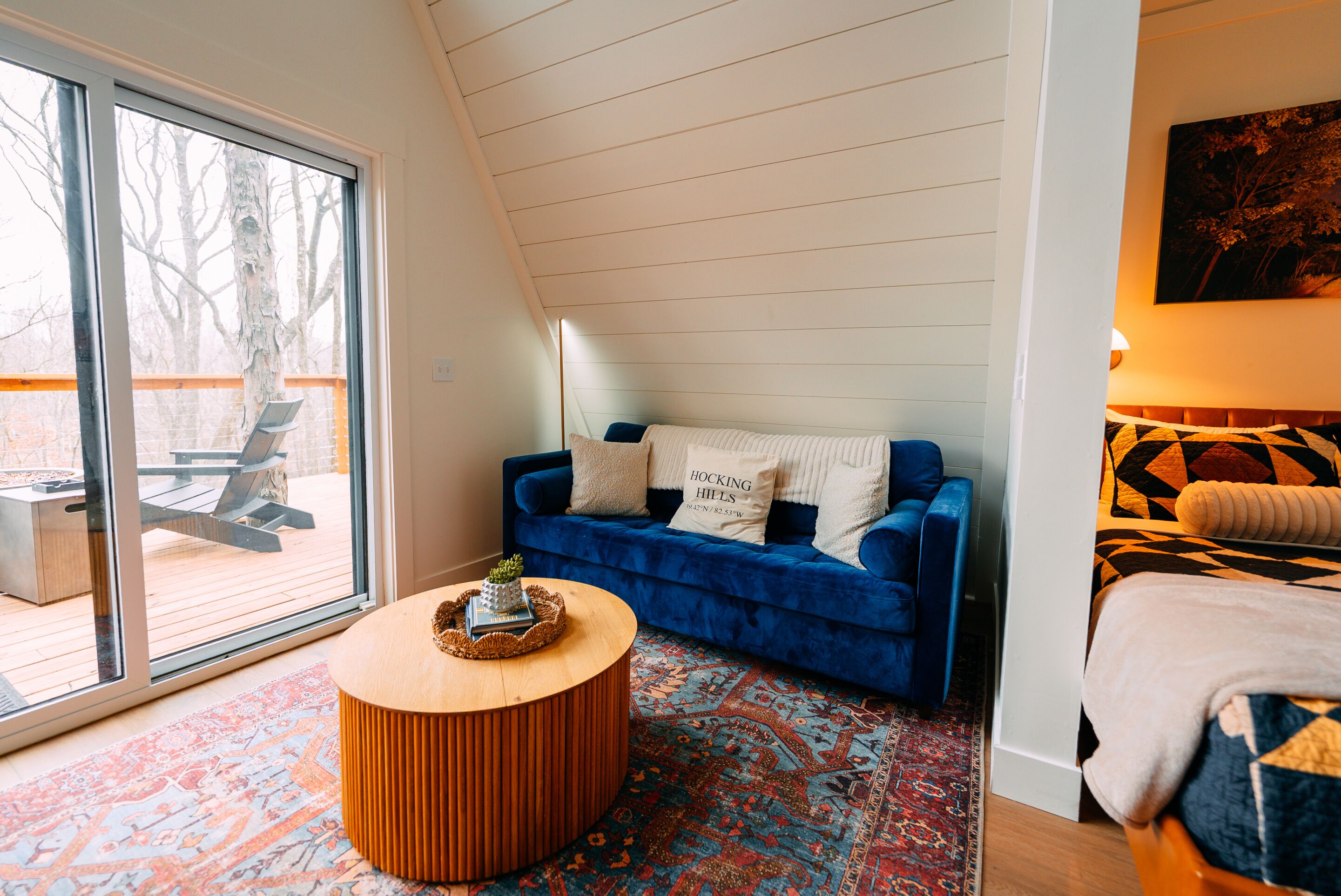 A room with a blue sofa, a round wooden coffee table, a patterned rug, and a large window.