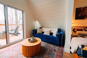 A room with a blue sofa, a round wooden coffee table, a patterned rug, and a large window. - Hickory Hollow | Hocking Hills, Hot Tub, Romantic (McArthur)