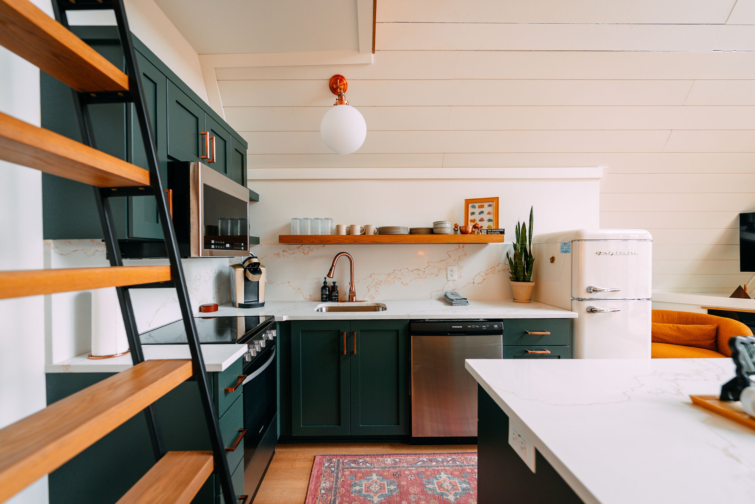 A kitchen with dark green cabinets, a white countertop, a stainless steel dishwasher, and a white refrigerator.