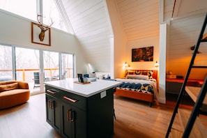 A modern interior with a loft-style ceiling, a central island with cabinets, a bed with a patterned bedspread, and a painting on the wall. - Hickory Hollow | Hocking Hills, Hot Tub, Romantic (McArthur)