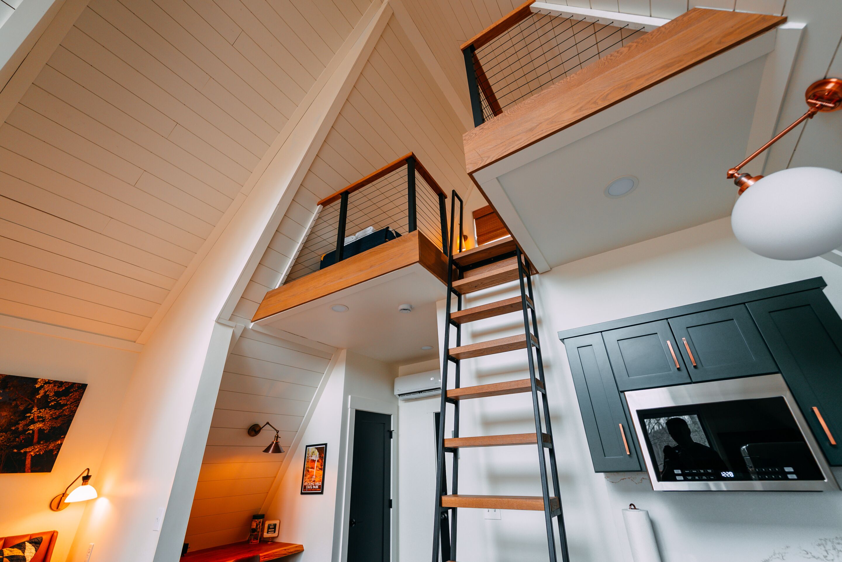 A loft-style kitchen with a wooden ladder, a built-in oven, and a mezzanine with a railing.