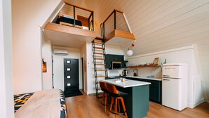 Un appartement de style « loft » comprenant une cuisine, un coin repas et une chambre avec un lit en mezzanine.