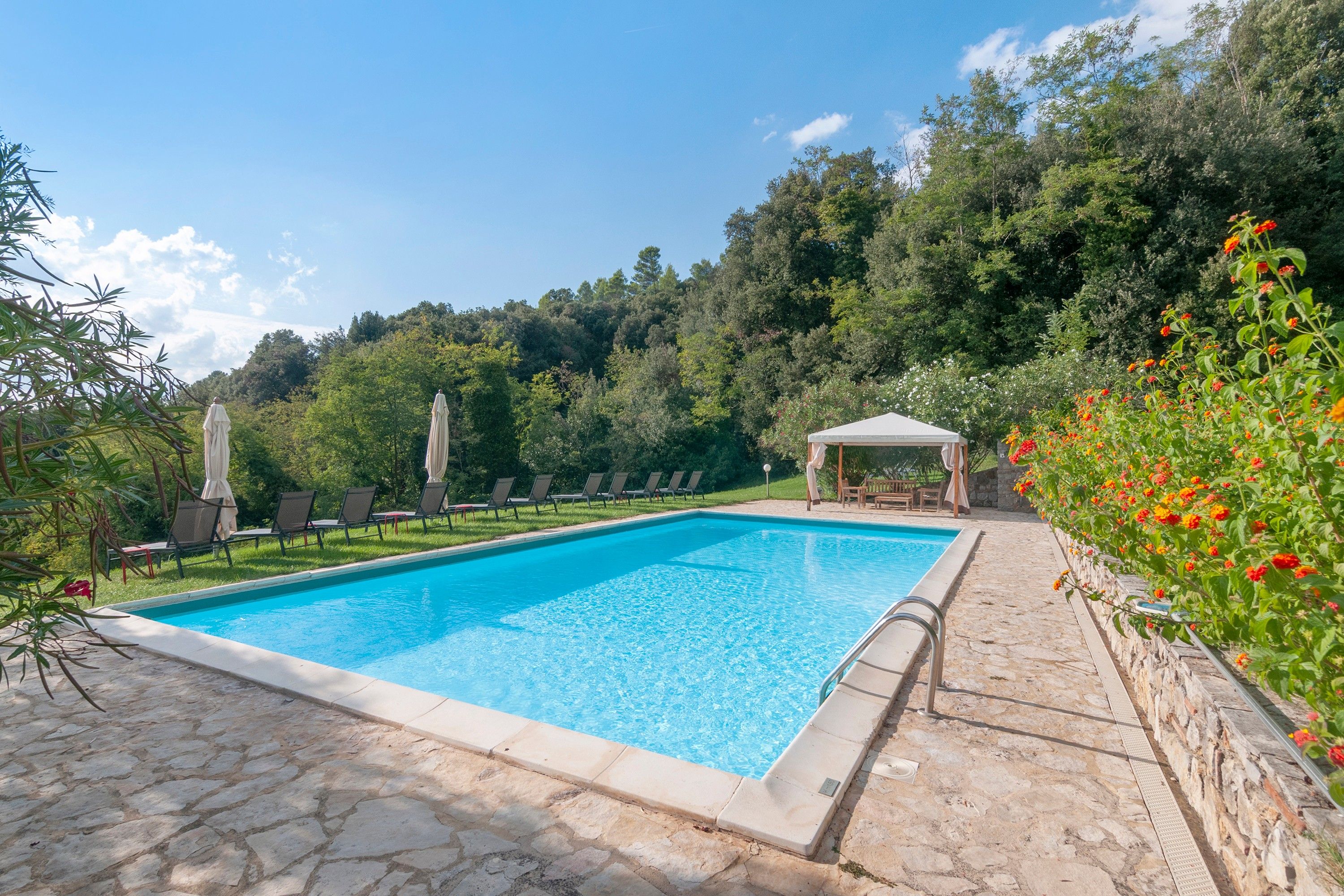 A rectangular swimming pool with clear blue water, surrounded by stone tiles.