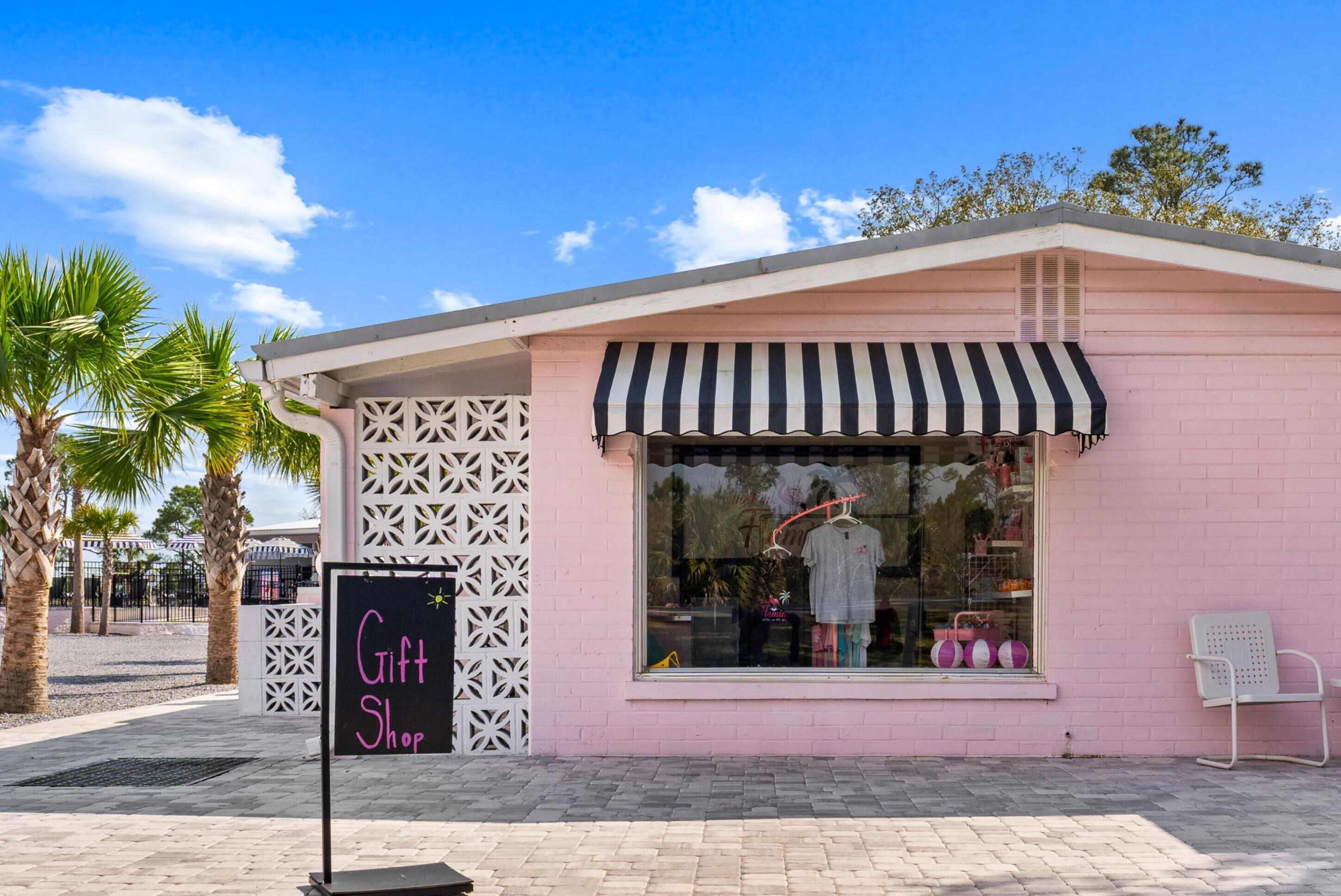 Un bâtiment rose avec un auvent rayé noir et blanc, une enseigne indiquant «Boutique de cadeaux» et une vitrine exposant divers articles.