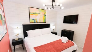 Un dormitorio con una cama grande, televisión, un cuadro y una araña.