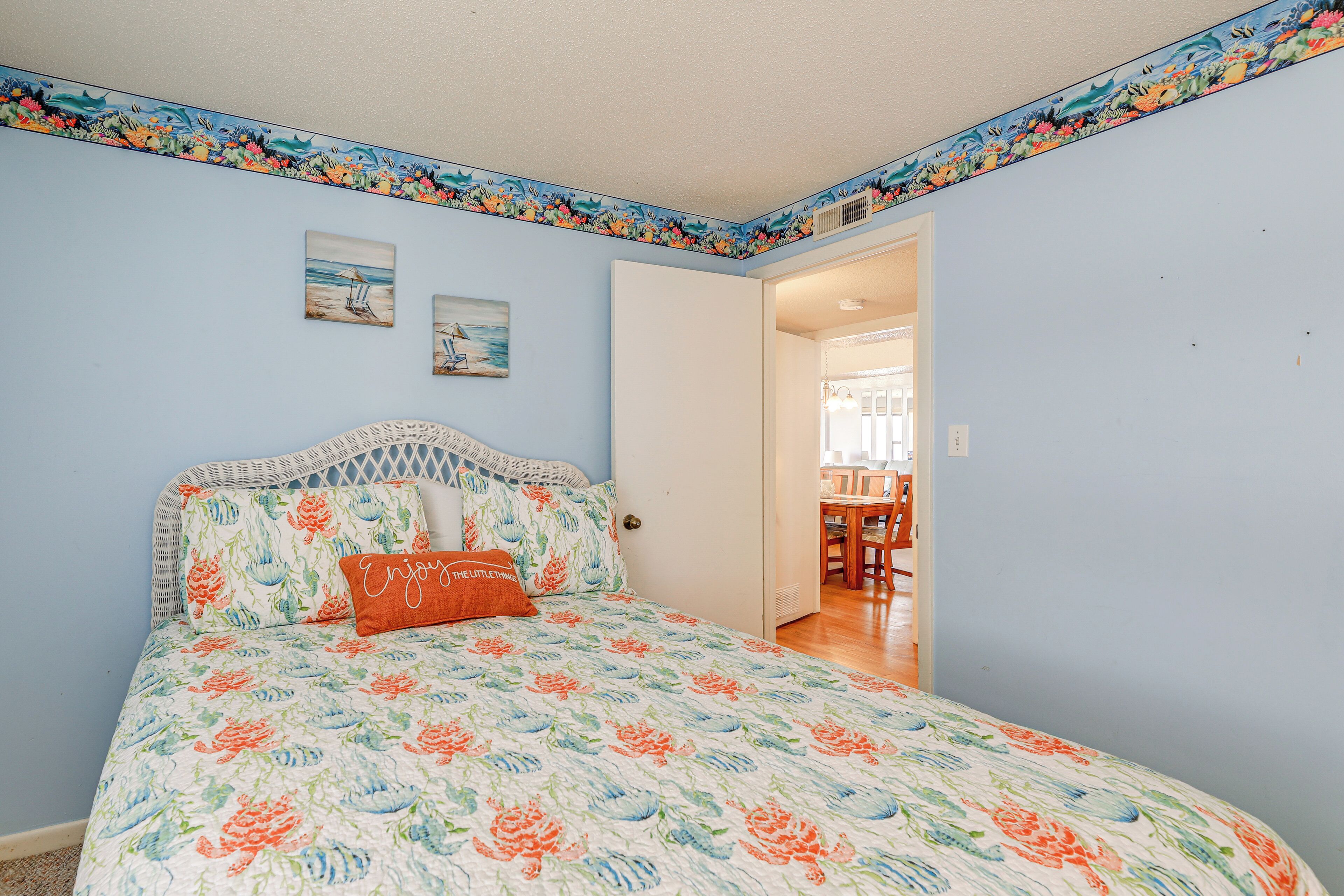 Une chambre à coucher avec une couvre-lit à motifs floraux, une tête de lit blanche et une porte donnant sur un coin repas.