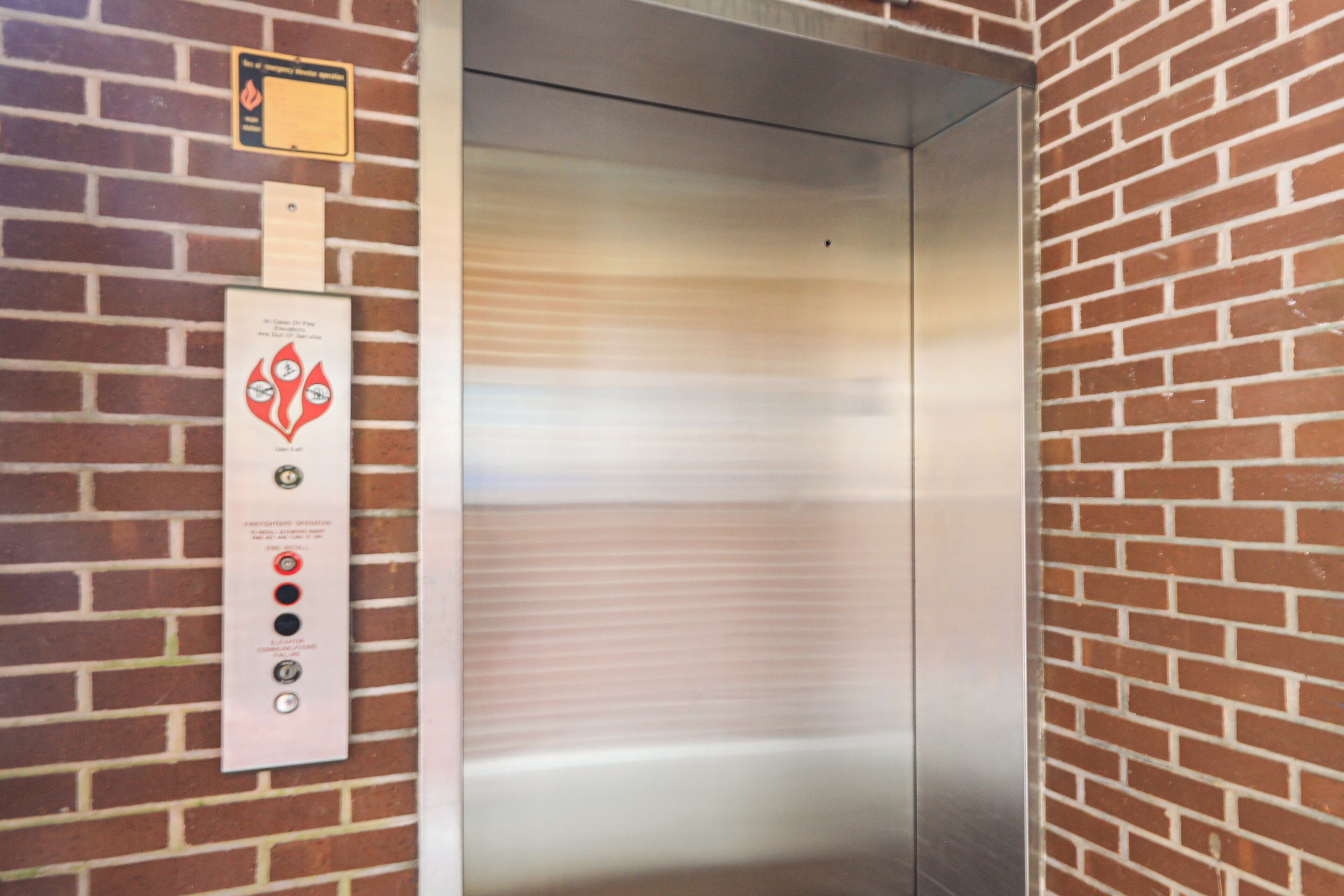 An elevator with a control panel featuring emergency instructions and a fire alarm button.