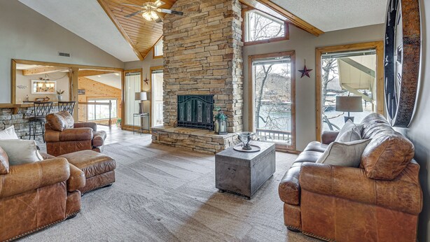 A spacious living area with leather sofas, a stone fireplace, and large windows. - Private Dual-slip Dock! Lake of the Ozarks Home (Gravois Mills)