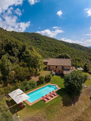 Une maison avec une piscine, entourée d’un paysage verdoyant et de collines.