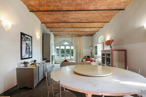 A dining area with a round table, chairs, and a kitchen in the background. - Villa Linchiano with Private Pool for 11 Guests (Gambassi Terme)