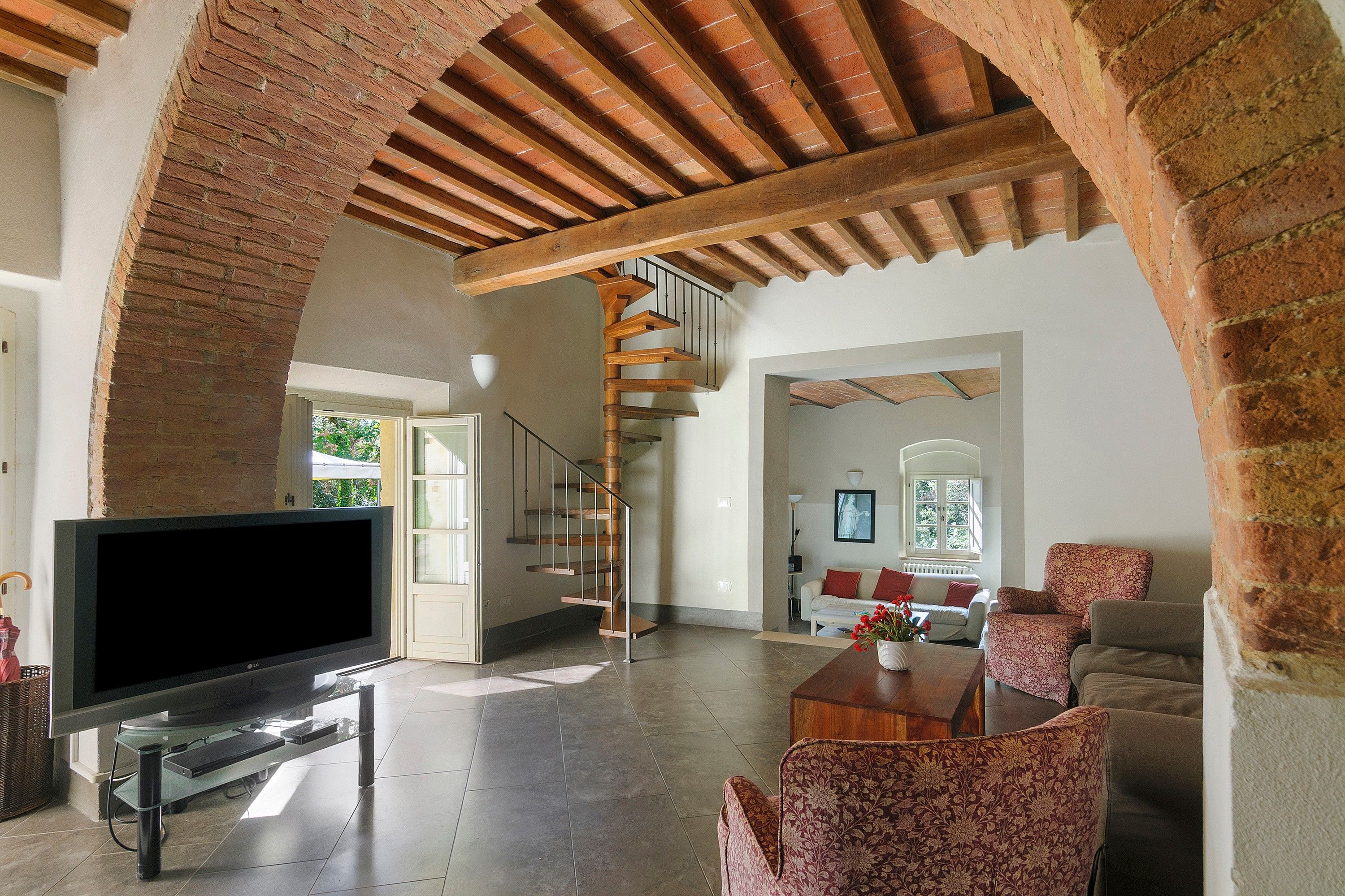 A spacious living area with a large flat-screen TV, a wooden staircase, and a cozy seating arrangement.