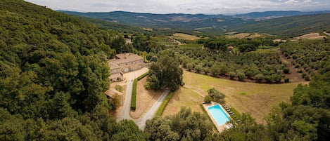 A villa with a swimming pool, surrounded by lush greenery and hills.