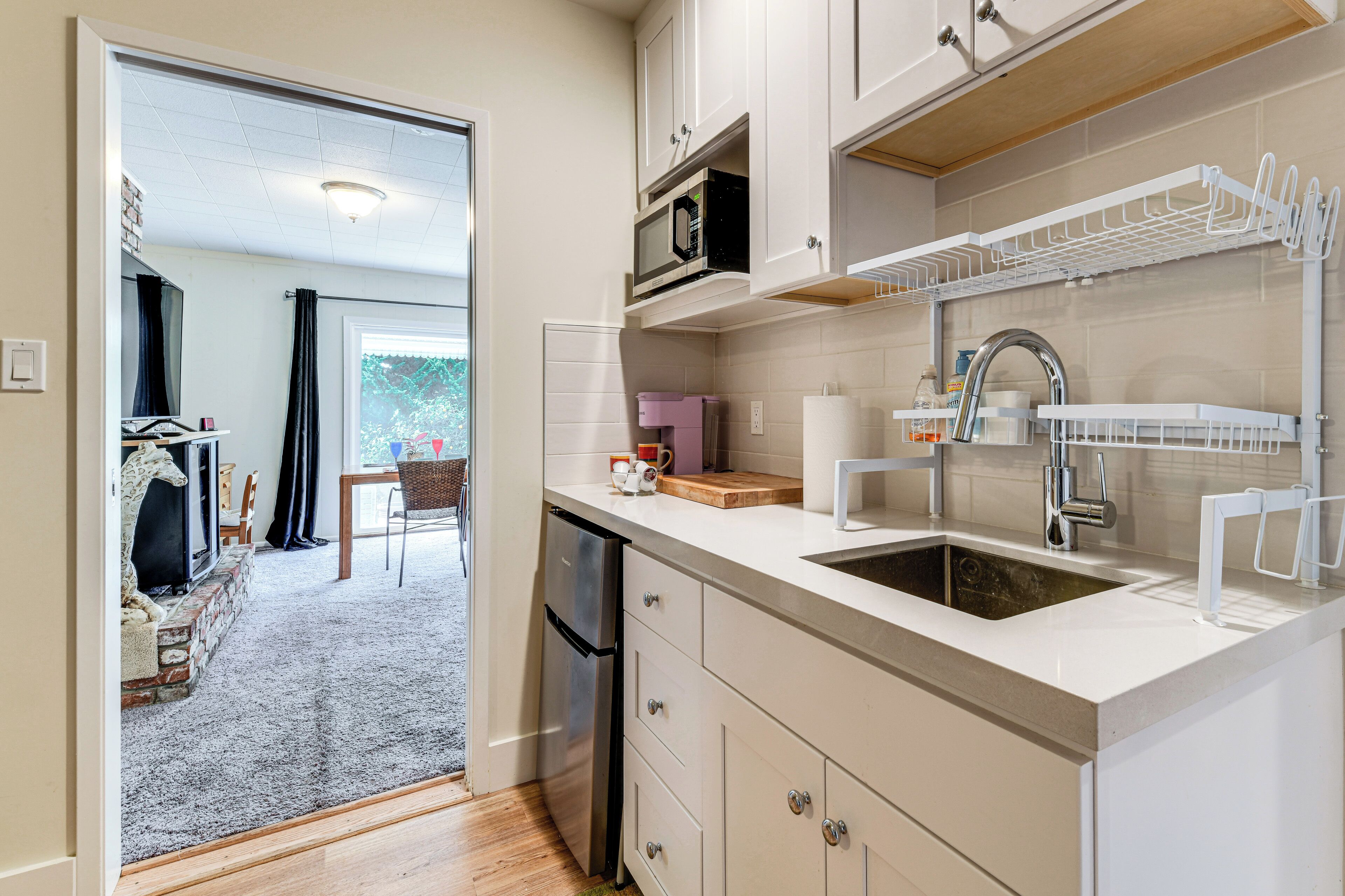 Una cocina moderna con armarios blancos, un refrigerador de acero inoxidable, un microondas integrado y un lavabo con escurreplatos.