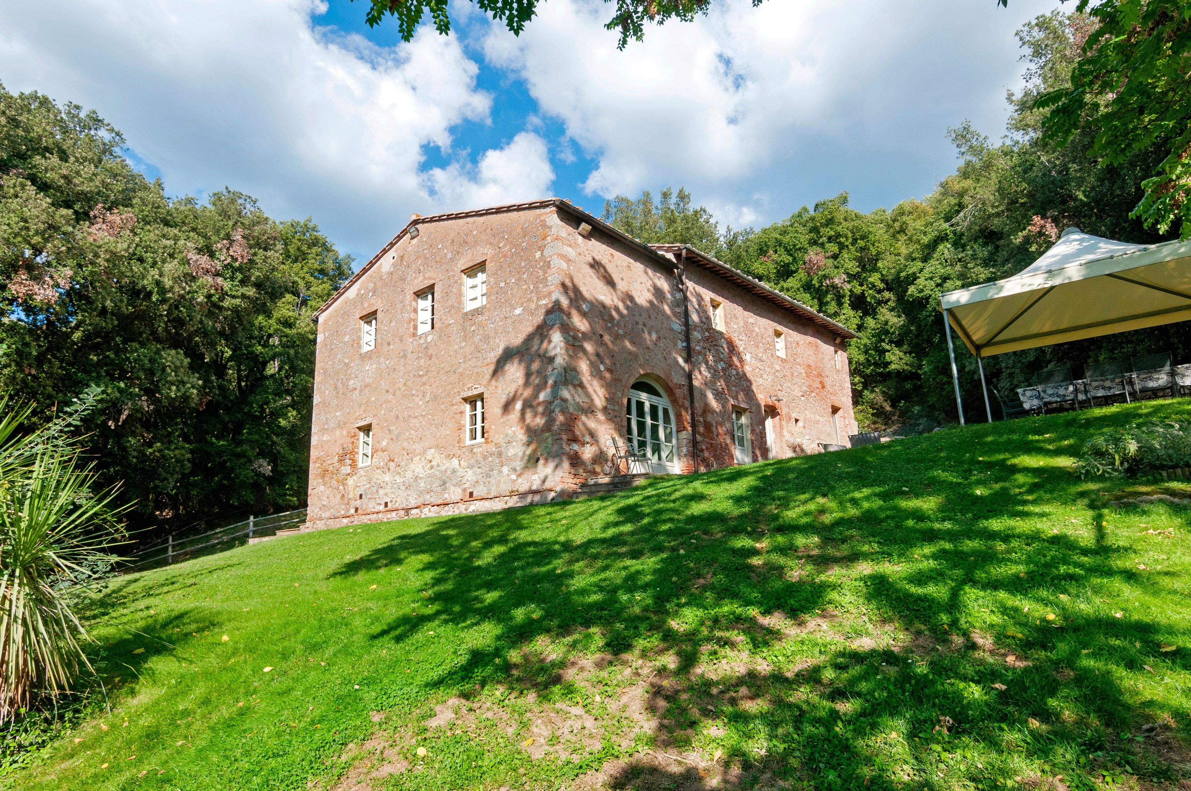 A rustic stone building with a sloped roof, surrounded by lush greenery and trees.