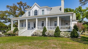 A two-story house with a porch, a chimney, and a well-maintained lawn. - On the Beach + Gulf: Luxe Pass Christian Escape (Pass Christian)