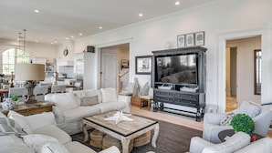 A spacious living room with a fireplace, comfortable seating, and a television. - On the Beach + Gulf: Luxe Pass Christian Escape (Pass Christian)