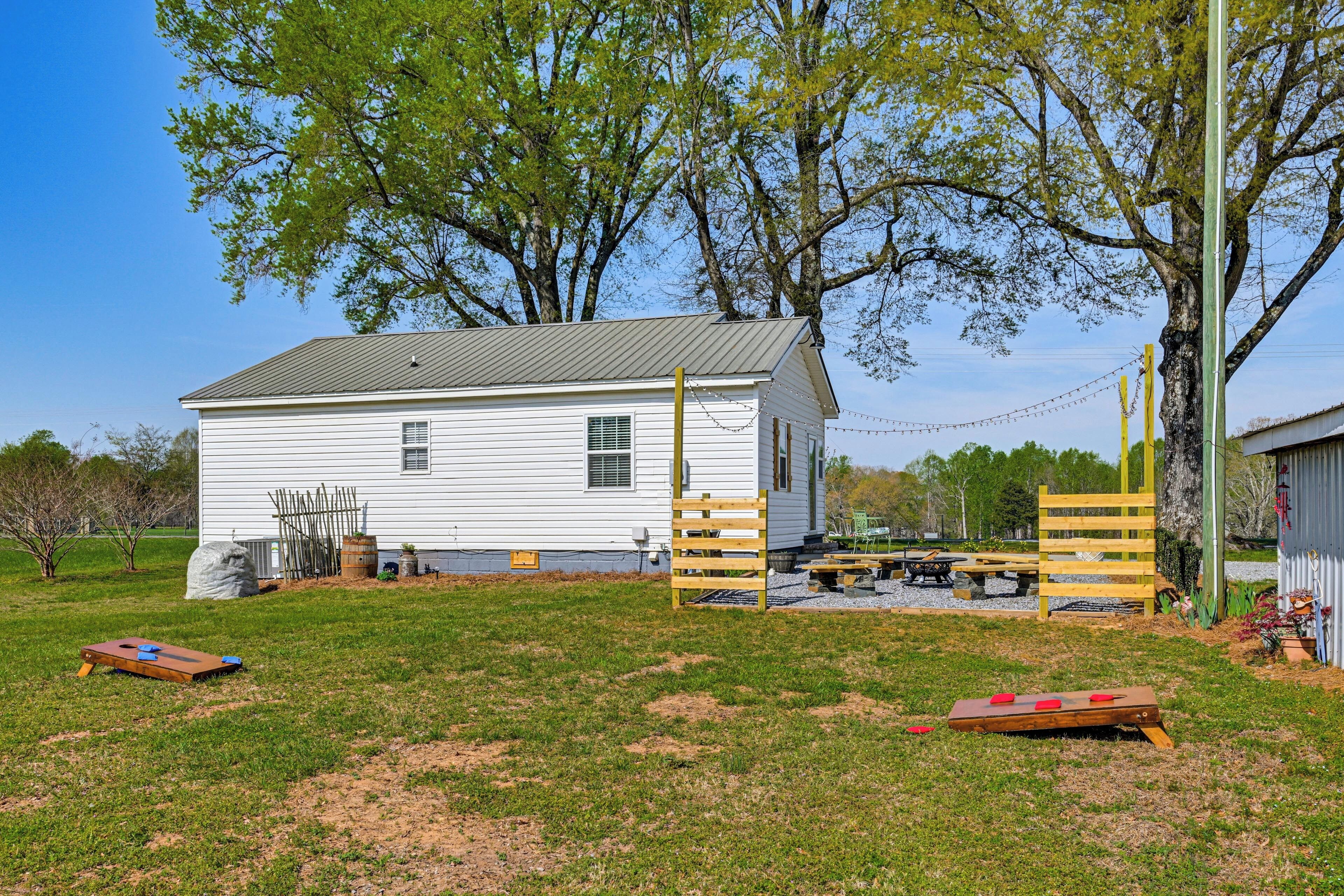 A white single-story house with a metal roof, a wooden deck, and a small garden area with trees and a picnic table.