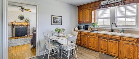 Una cocina con armarios de madera, una mesa de comedor con sillas, un ventilador de techo y un letrero de bienvenida.