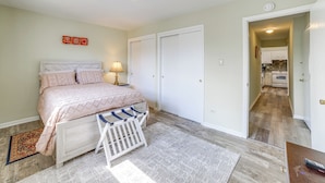 A bedroom with a bed, bedside table, lamp, and a view into the kitchen. - Cozy Couples Escape in Homewood: Pets Welcome! (Homewood)