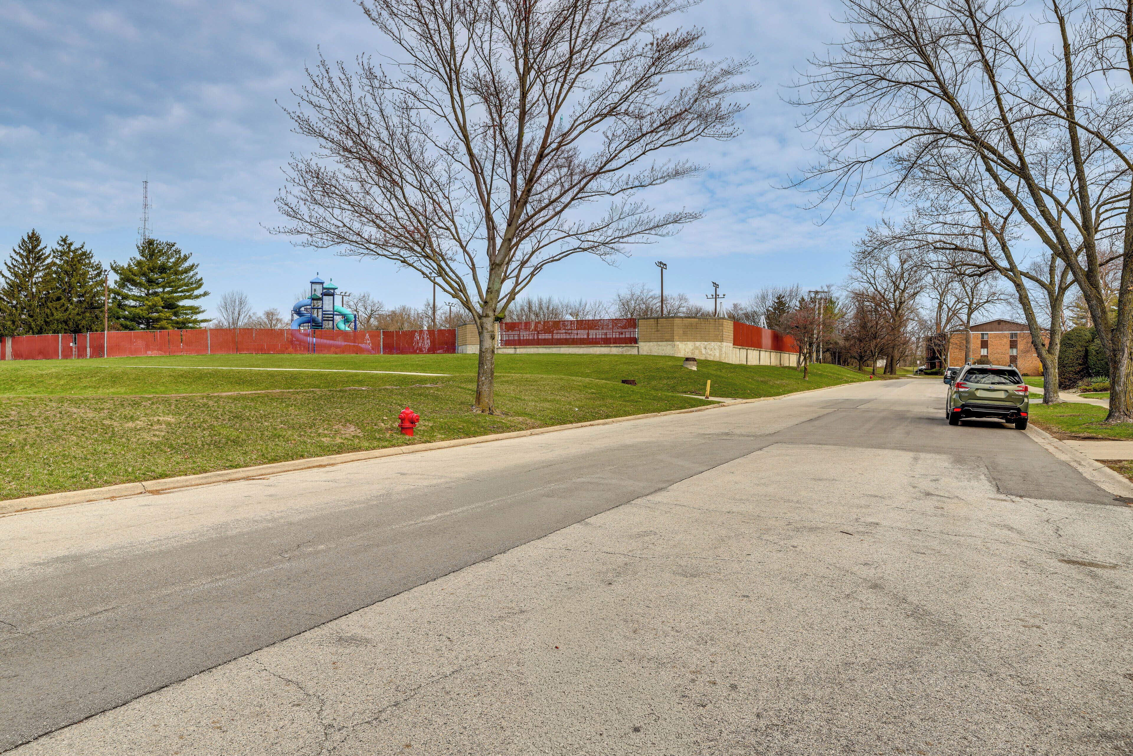 A street with a green field, a red fire hydrant, and a building in the background.