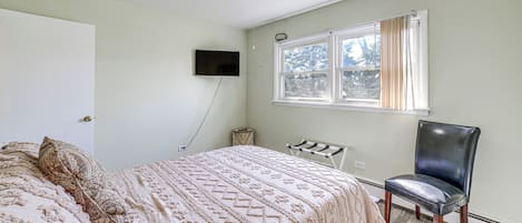 Un dormitorio con cama, una silla, ventilador de techo, ventana con cortinas y televisor fijado a la pared.
