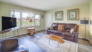A living room with a leather sofa, a coffee table, a TV, and a large window. - Cozy Couples Escape in Homewood: Pets Welcome! (Homewood)