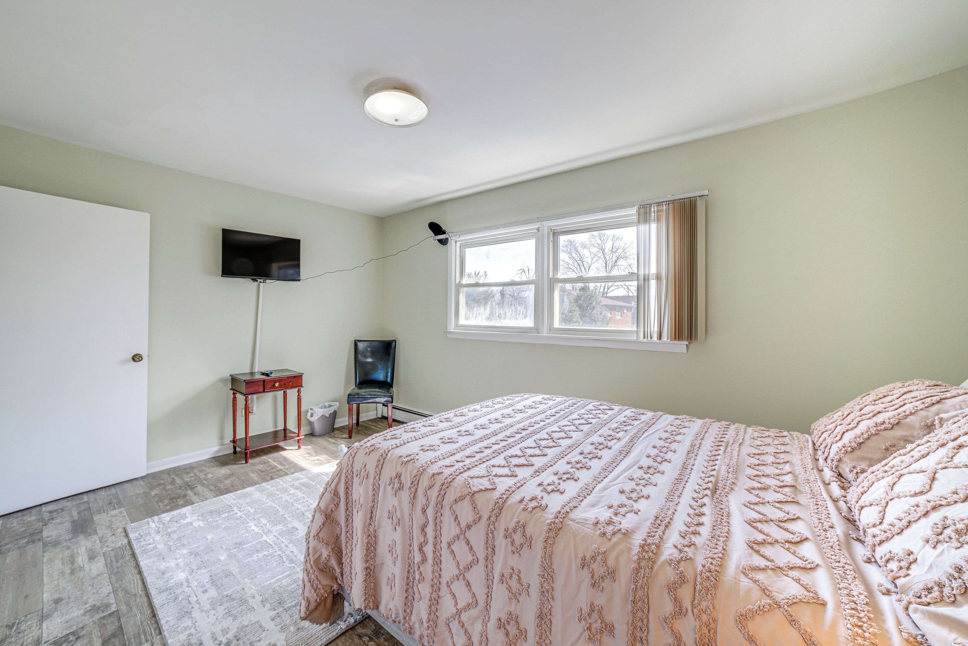 A bedroom with a bed, a television, a chair, and a window.