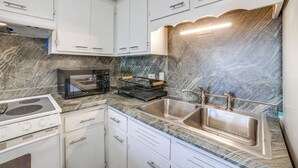 A kitchen with white cabinets, a stainless steel sink, a built-in microwave, and a stove. - Cozy Couples Escape in Homewood: Pets Welcome! (Homewood)