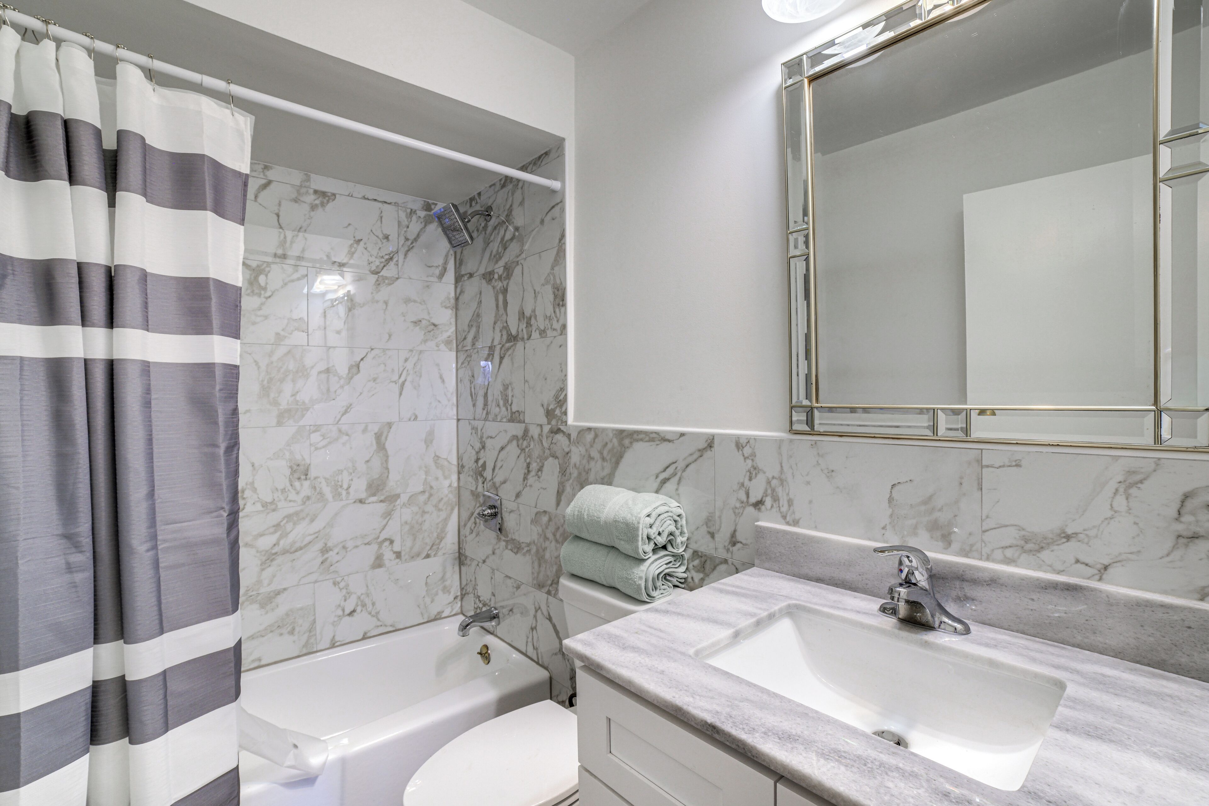 Une salle de bain avec une baignoire, des toilettes et un lavabo double doté d’un plan de travail en marbre.