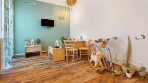 Ein Zimmer mit Holzboden, einem Schreibtisch mit Stühlen, einem an der Wand befestigten Fernseher und einer Pendelleuchte.