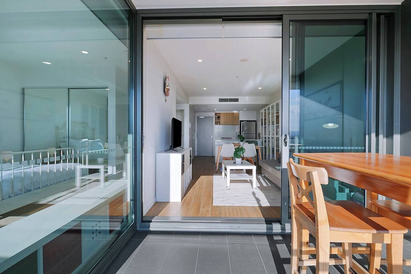 A modern interior with a glass door leading to a dining area, a kitchen in the background, and a visible TV.
