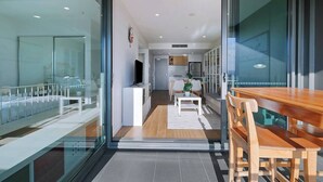 Ein modernes Interieur mit einer Glastür, die in einen Essbereich führt, einer Küche im Hintergrund und einem sichtbaren Fernseher.