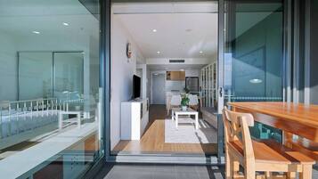 A modern interior with a glass door leading to a dining area, a kitchen in the background, and a visible TV.