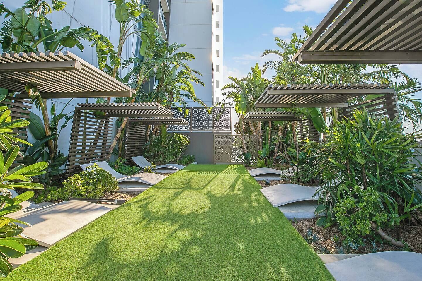 A well-maintained garden with a central lawn, surrounded by various tropical plants and wooden pergolas.